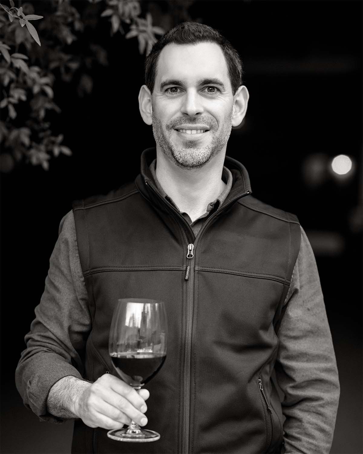 Black and White photo of Sebastian Donoso smiling at camera and holding wine glass
